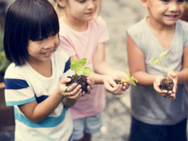 Discuss disability with child | Neuromyelitis News | Stock photo of three young children holding handfuls of soil with green sprouts.