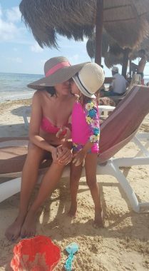 mental health | Neuromyelitis News | Jennifer sits on a lounge chair on the beach in Mexico wearing a bathing suit and a floppy hat. Her daughter is standing next to her and giving her a kiss on the cheek.