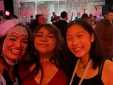 NMO Awareness Gala | Neuromyelitis News | Candice Galvan, Bella Damian-Ortiz, and Nella Choi smile for a selfie at the NMO Awareness Gala. They are dressed up and adorned in fun accessories, and a crowd of people dances behind them.