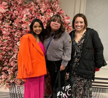 NMO Awareness Gala | Neuromyelitis News | Bella Damian-Ortiz and Candice Galvan meet Sumaira Ahmed in person for the first time at The Sumaira Foundation's ambassador dinner. The three women are dressed up, smiling, and posing in front of a wall of pink flowers.