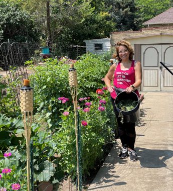 chronic illness mental health | Neuromyelitis News | Candice stands next to a lush garden holding a bucket of either weeds or vegetables. She's smiling, and it's a bright and sunny day
