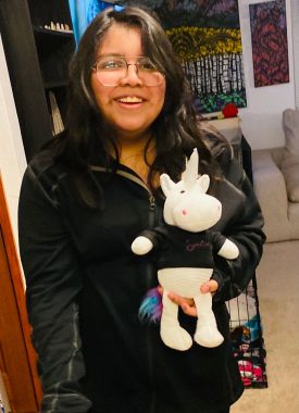 nmo children | Neuromyelitis News | Candice's daughter Bella smiles while holding a white unicorn with colored hair, which was sent to her by The Sumaira Foundation.