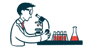 A scientist looks into a microscope in a laboratory, alongside a rack of vials and a flask.